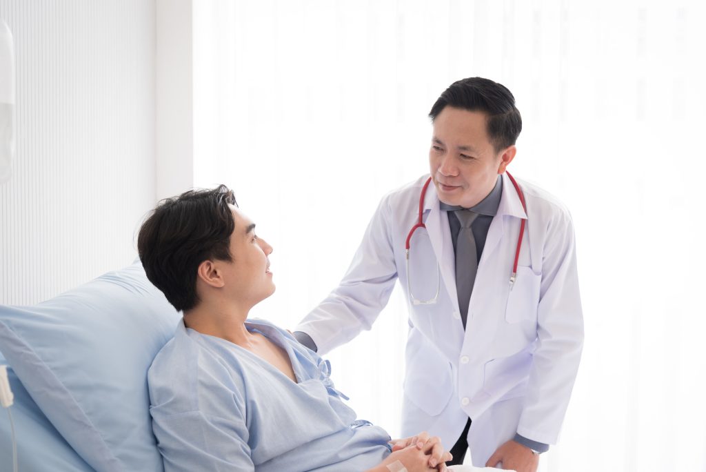doctor talking to a male patient lying in a hospital bed