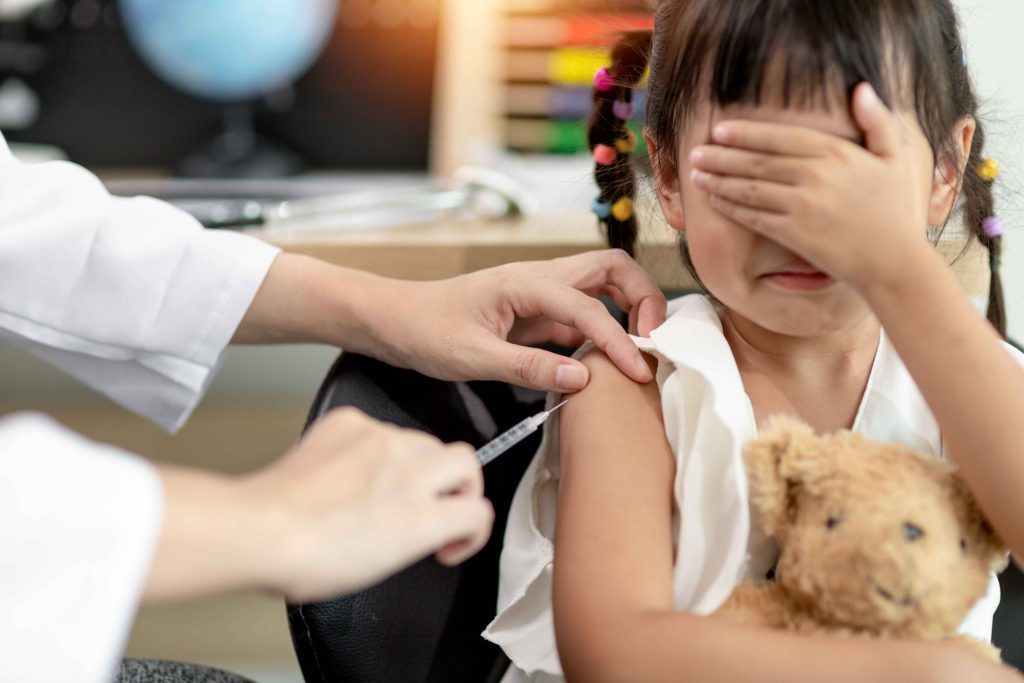 little girl given an injection while holding her plush toy