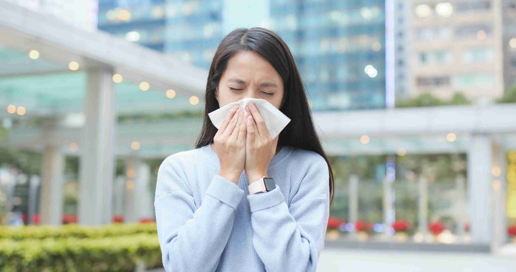 woman with runny nose due to flu standing outdoors