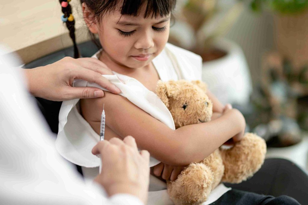Young girl holding a teddy bear while getting immunized.